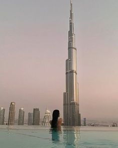 a woman is sitting in the pool looking at the burj