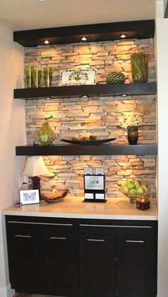 a kitchen with black cabinets and stone wall behind the counter top, along with lights on