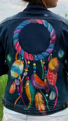 a woman wearing a denim jacket with colorful feathers painted on the front and back of it