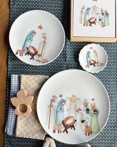 three plates with nativity scenes painted on them sitting on a blue and white table cloth