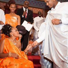 a woman in an orange dress sitting next to a man wearing a white suit and tie