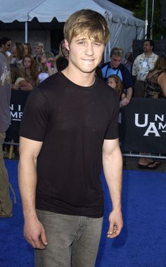 a young man standing in front of a crowd on a blue carpet with people looking at the camera