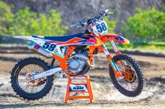 an orange and blue dirt bike parked on top of a small stand in the dirt