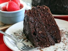 a piece of chocolate cake on a plate with a fork and bowl of strawberries