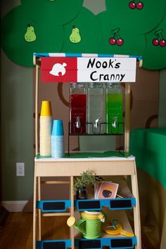 there is a wooden cart with cups and other items on it in front of a green wall