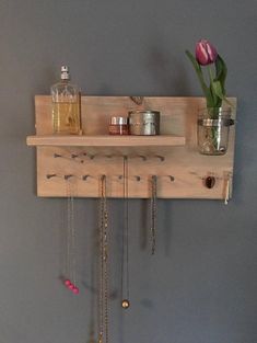 a wooden shelf with jewelry hanging from it's sides and a flower in a vase on top