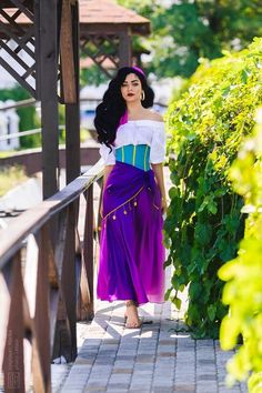 a woman in a purple and blue dress is standing on a walkway near some bushes