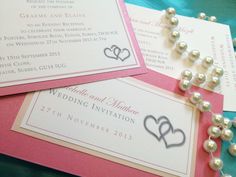 three wedding stationery cards with pearls attached to them on a blue and pink table cloth