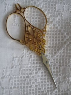 a pair of gold scissors sitting on top of a white tablecloth covered with lace