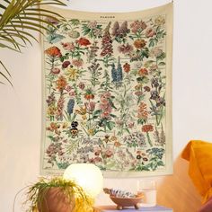 a tapestry hanging on the wall next to a table with a lamp and potted plant