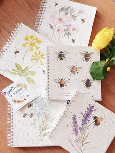 four notebooks with flowers and bees on them sitting next to a yellow flower bouquet