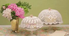 two white doily covered cakes sitting on top of a table next to a vase with pink flowers