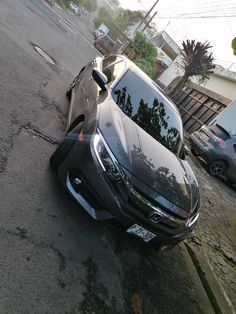 a black car parked on the side of a road next to a tree and fence