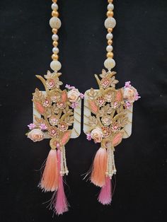 two necklaces with flowers and tassels hanging from the side on a black background