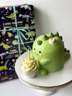 a green dinosaur cake sitting on top of a white plate next to a gift bag