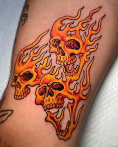 a close up of a person's leg with tattoos on it and two skulls in flames