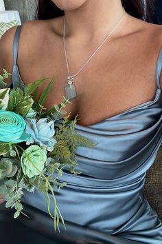 a woman in a blue dress holding a bouquet of flowers and wearing a silver necklace