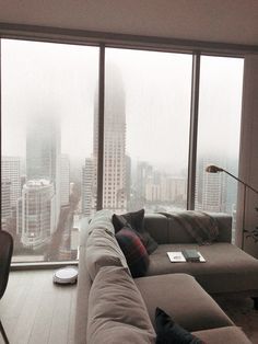 a living room filled with furniture next to tall buildings in the foggy cityscape