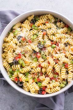 a white bowl filled with pasta salad on top of a blue cloth next to a fork