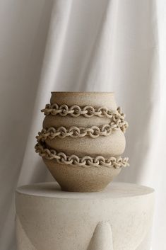 a white vase sitting on top of a table with chains around it's base