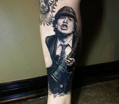 a person with a tattoo on their leg holding a guitar and wearing a suit, tie and hat