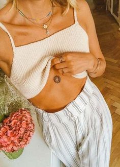 a woman with tattoos on her stomach sitting next to a flower pot and some flowers