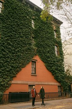 two people walking past an orange building covered in ivy