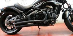 a black motorcycle parked on top of a red tile floor next to a white wall