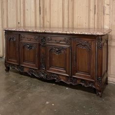 an old wooden sideboard with marble top and carvings on the doors, in front of a wood paneled wall