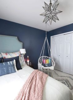 a bedroom with blue walls, white bedding and a hammock hanging from the ceiling