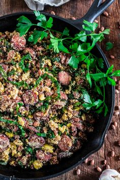 a skillet filled with meat and vegetables on top of a wooden table next to garlic