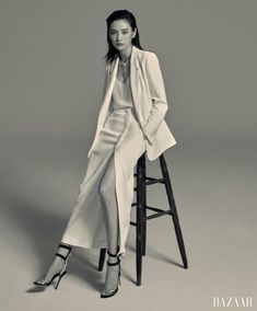 a woman sitting on top of a stool wearing a white coat and high heeled shoes