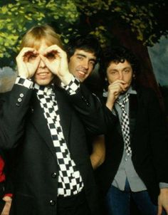 three young men standing next to each other in front of a tree with their hands covering their eyes