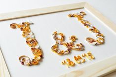 the word love spelled in gold letters on a white background with wooden frame and bead work