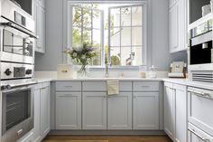 a kitchen with white cabinets and wooden flooring next to an open window that has flowers in it