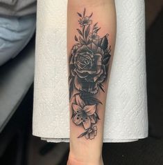 a black and white rose tattoo on the left arm, with flowers in the center