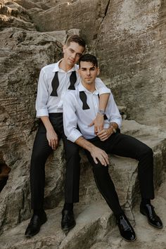 two young men sitting on some rocks wearing ties and dress shirts with their arms around each other