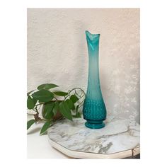 a blue vase sitting on top of a marble table next to a potted plant