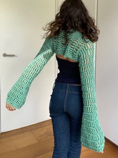 a woman standing in front of a door wearing jeans and a green knitted sweater