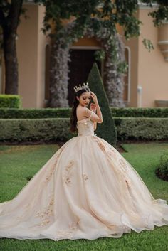 a woman in a ball gown standing on the grass with her hands behind her head