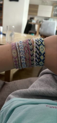 a woman's arm with several bracelets on it and a glass in the background