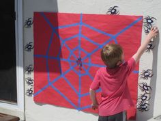 a young boy painting a spider web on the side of a building with blue and red paint