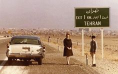 two women standing in front of a car on the side of a road near a sign