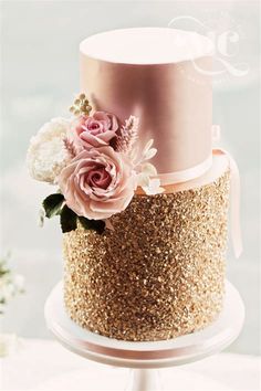 a three tiered cake with pink flowers on top and gold sequins around the edges