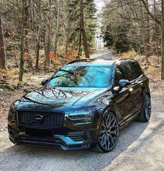 a black volvo car parked on the side of a road in front of some trees