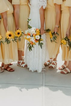 a group of women standing next to each other in yellow dresses and sandals holding bouquets