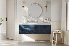 a bathroom with blue cabinets and a round mirror on the wall over the sink, along with a stool