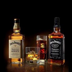 three bottles of jack daniels whiskey and two glasses with ice cubes on the table