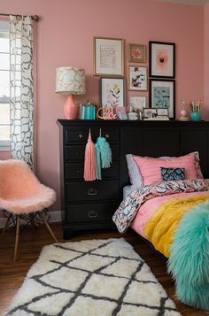 a bedroom with pink walls, black dresser and colorful bedding in the corner area