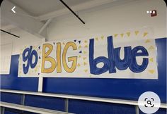 a big blue sign hanging from the side of a wall in a room with white and blue walls